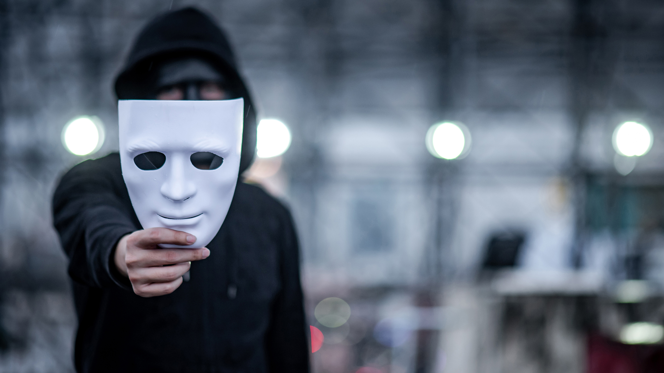 Mystery hoodie man with black mask holding white mask in his hand. 