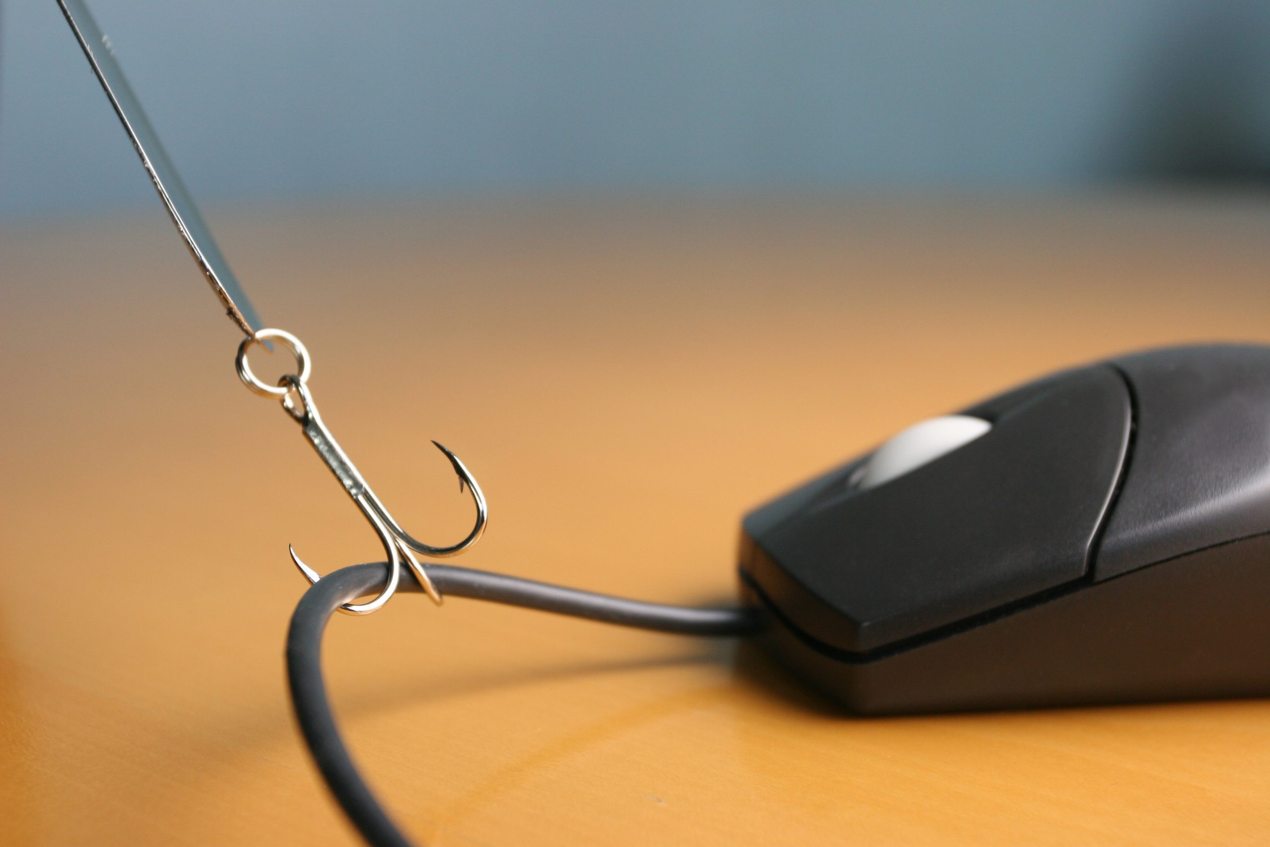 Close up of fishing hook snagging a computer mouse cord on a desktop.