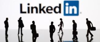 Human figurines standing in front of Apple iPad monitor displaying LinkedIn logo.