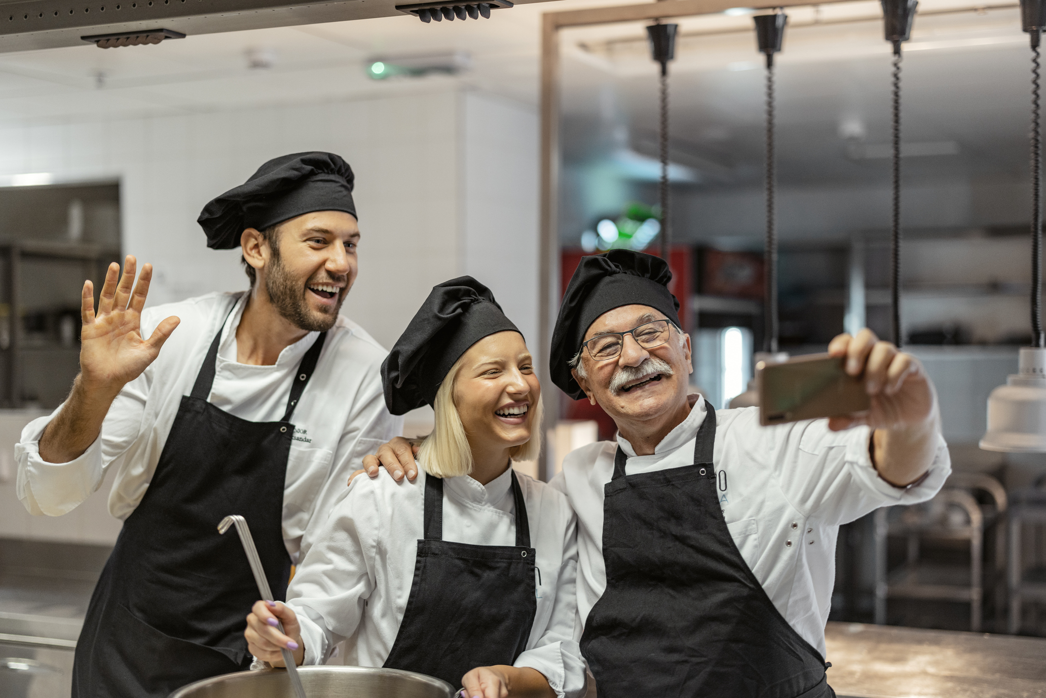 Senior male chef make selfie while working in a modern kitchen with his staff