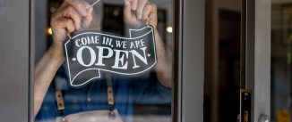 Close-up on a business owner hanging an open sign on the door of his restaurant - food and drink establishment concepts