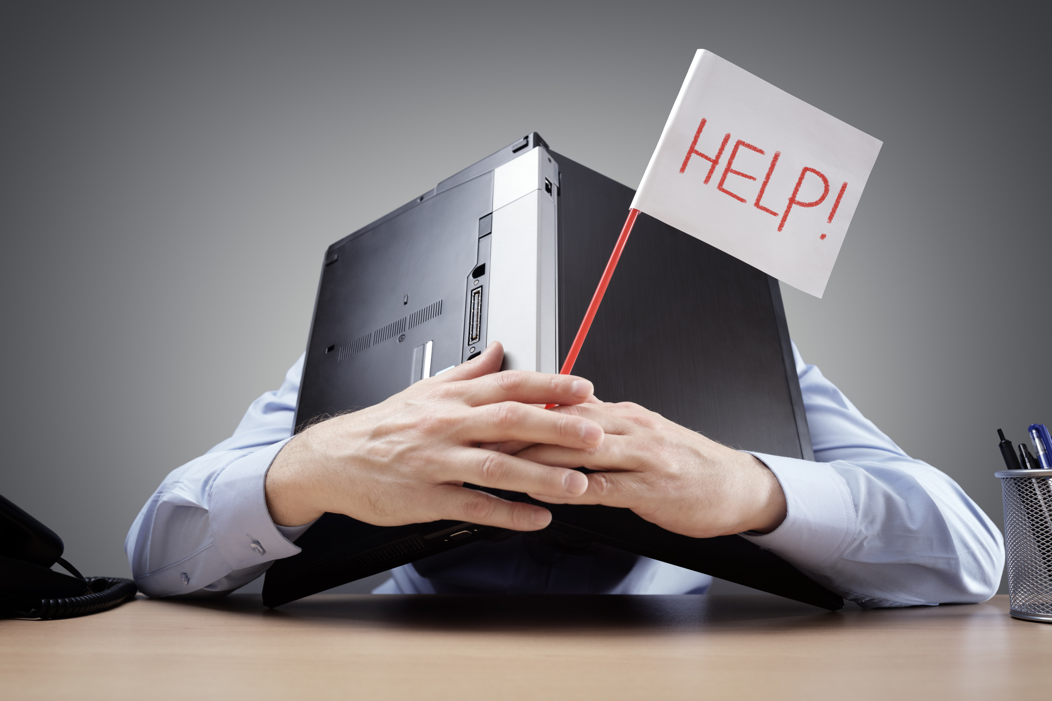 Frustrated and overworked businessman burying his head uner a laptop computer asking for help