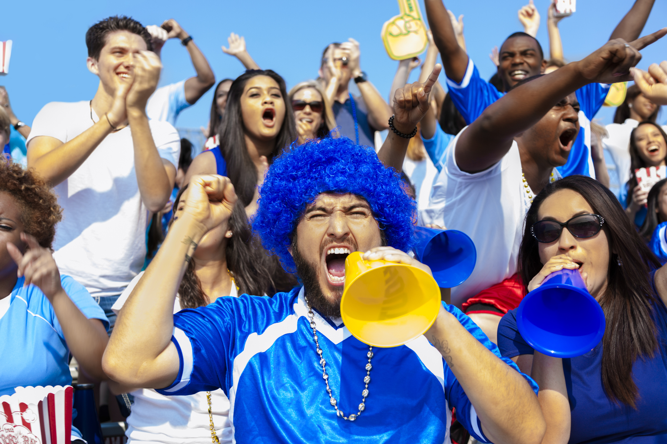 Multi-ethnic group of fans scream and yell for their team to win during a local sports event.