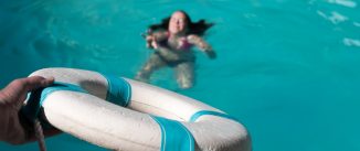 Man holding out life preserver to help young woman who is drowning in a swimming pool. Rescuing woman drowning in pool, focus on the lifesaver.