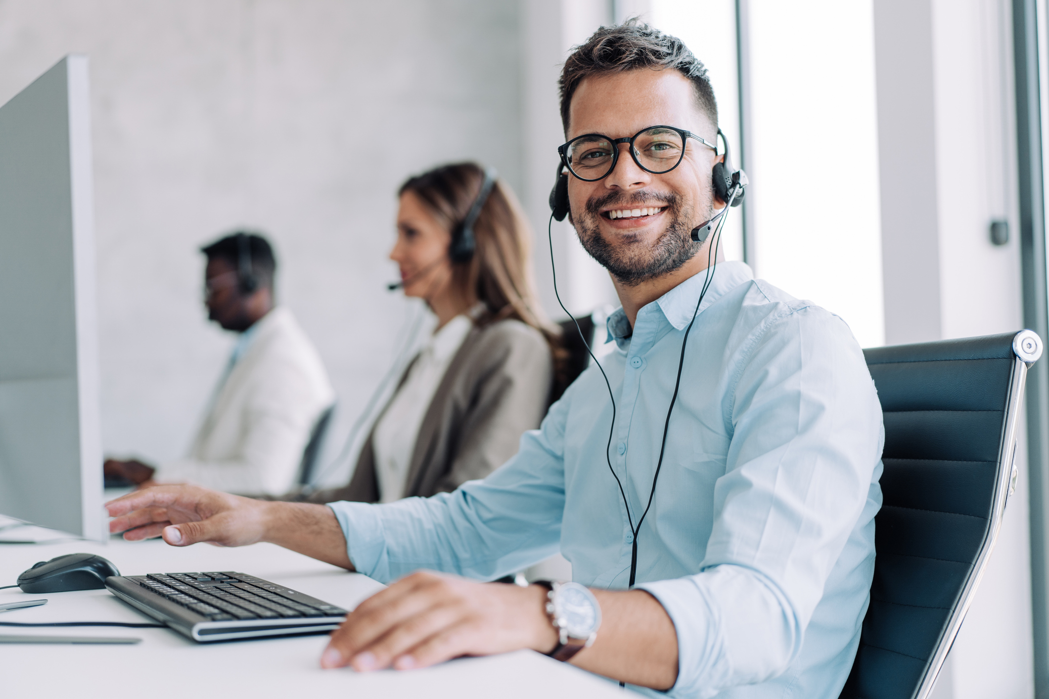 Shot of call center operators working in the office. Call center agent working with his colleagues in modern office. Smiling handsome businessman working in call center.