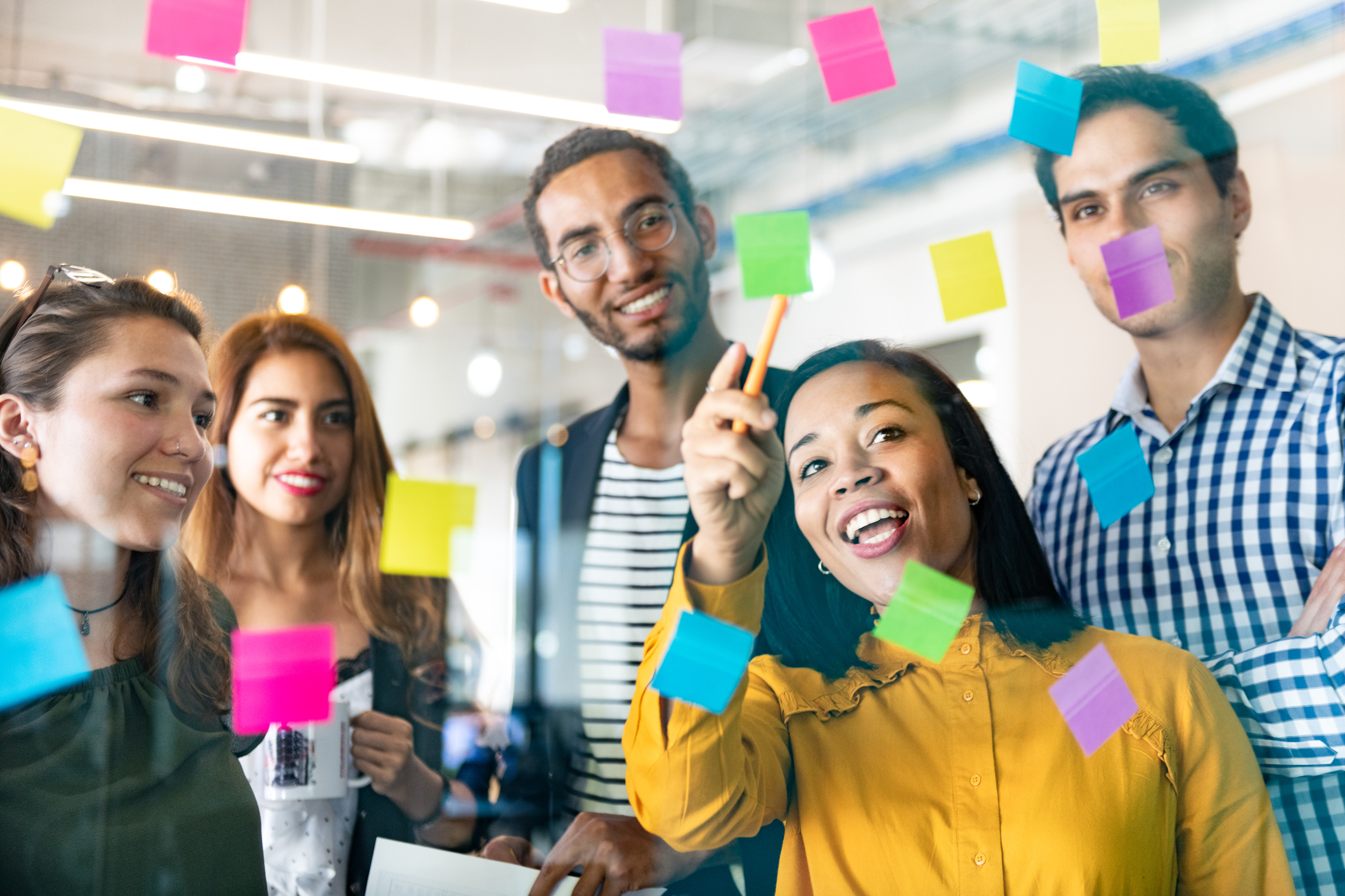 Young professionals planning tasks on glass wall with adhesive notes in co-working office