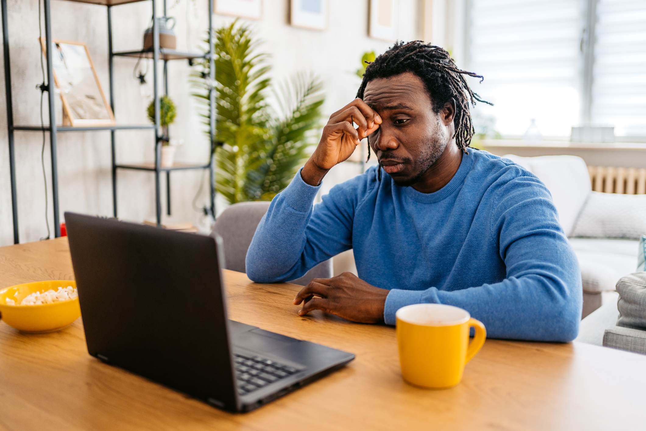 Tired young black handsome man working from home on a laptop and having a headache.