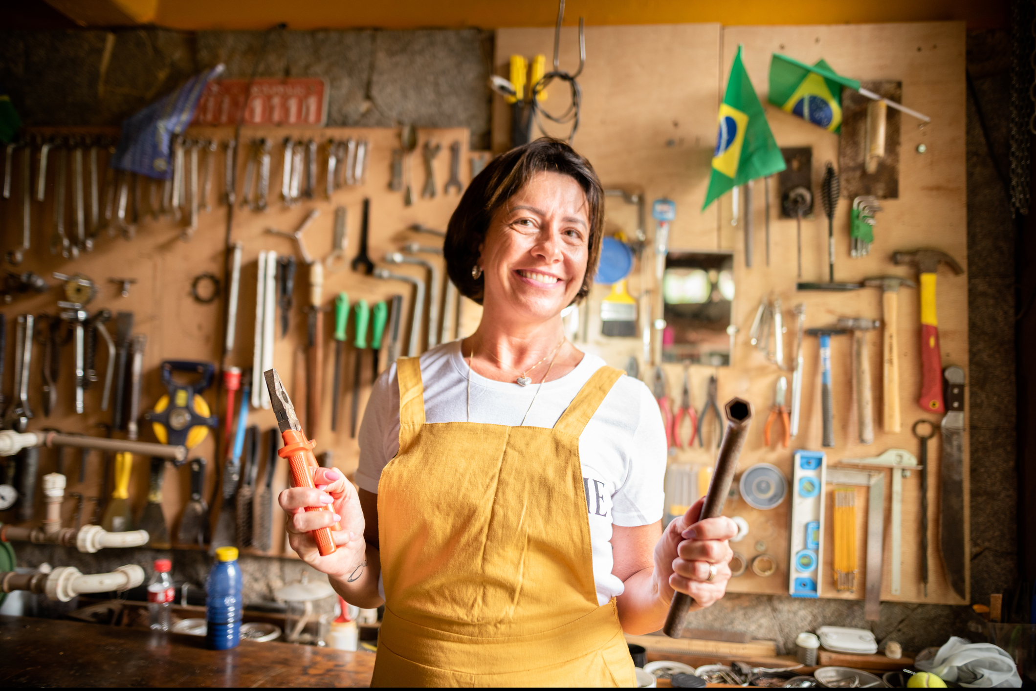 Portrait of a smiling mature woman in coveralls holding tools for a diy project in her garage at home
