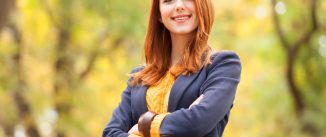 Redhead girl standing in nature with autumn leaves behind her