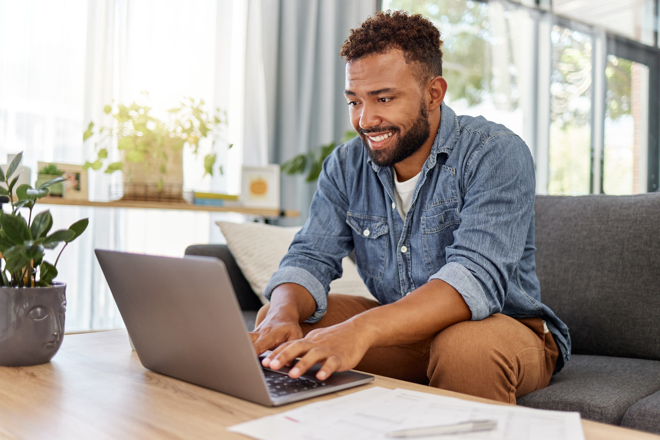 Young mixed race man working on filling out forms while typing on a laptop at home. One hispanic man planning and sending an email alone in the lounge at home