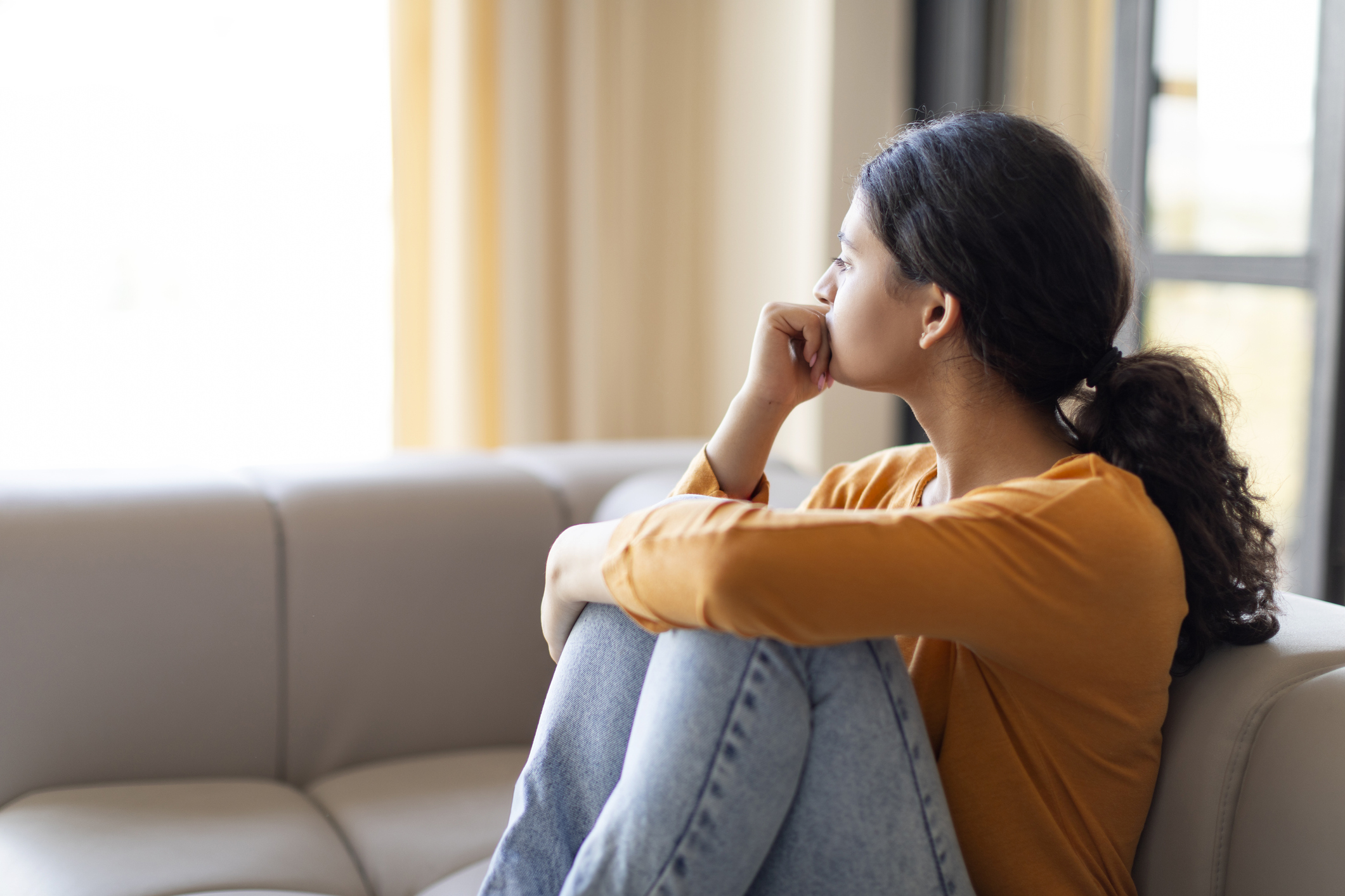 Portrait Of Pensive Depressed Young Indian Woman Sitting On Couch At Home, Upset Eastern Female Leaning Head On Hand And Looking Away, Suffering Mental Breakdown Or Seasonal Depression, Copy Space