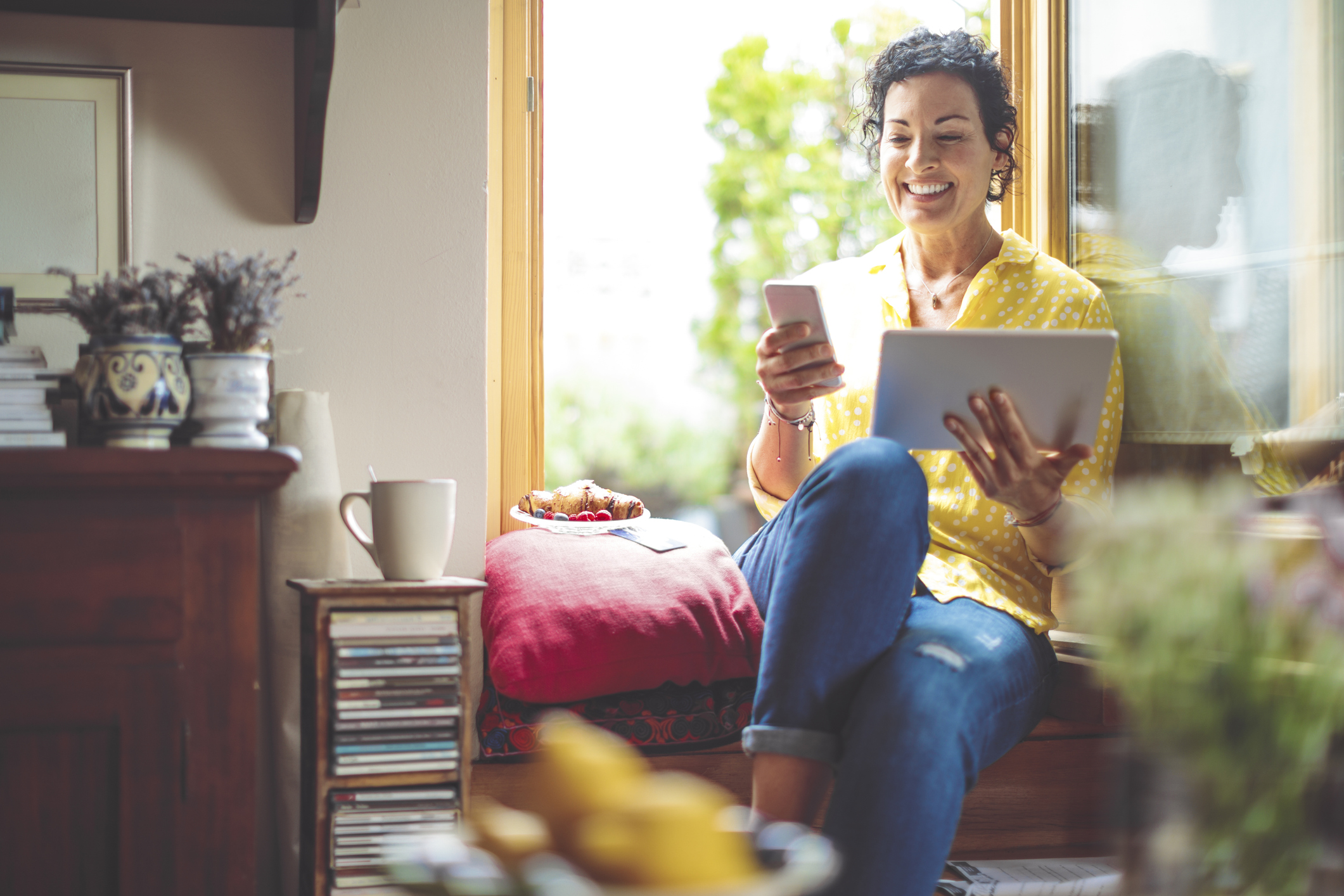 Mature woman is purchasing online, while seated at home with a laptop and a cellphone