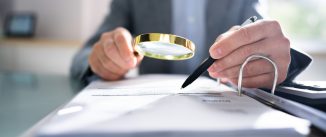 Close-up Of A Businessperson's Hand Looking At Receipts Through Magnifying Glass At Workplace