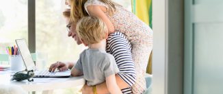 Children (4-5, 6-7) climbing on their mother while she works from home