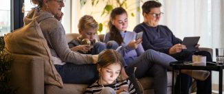 Parents sitting with children while using wireless technologies in living room at modern home