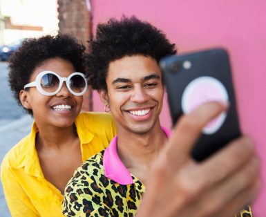 A young couple wearing yellow clothes taking a selfie in front of a pink wall