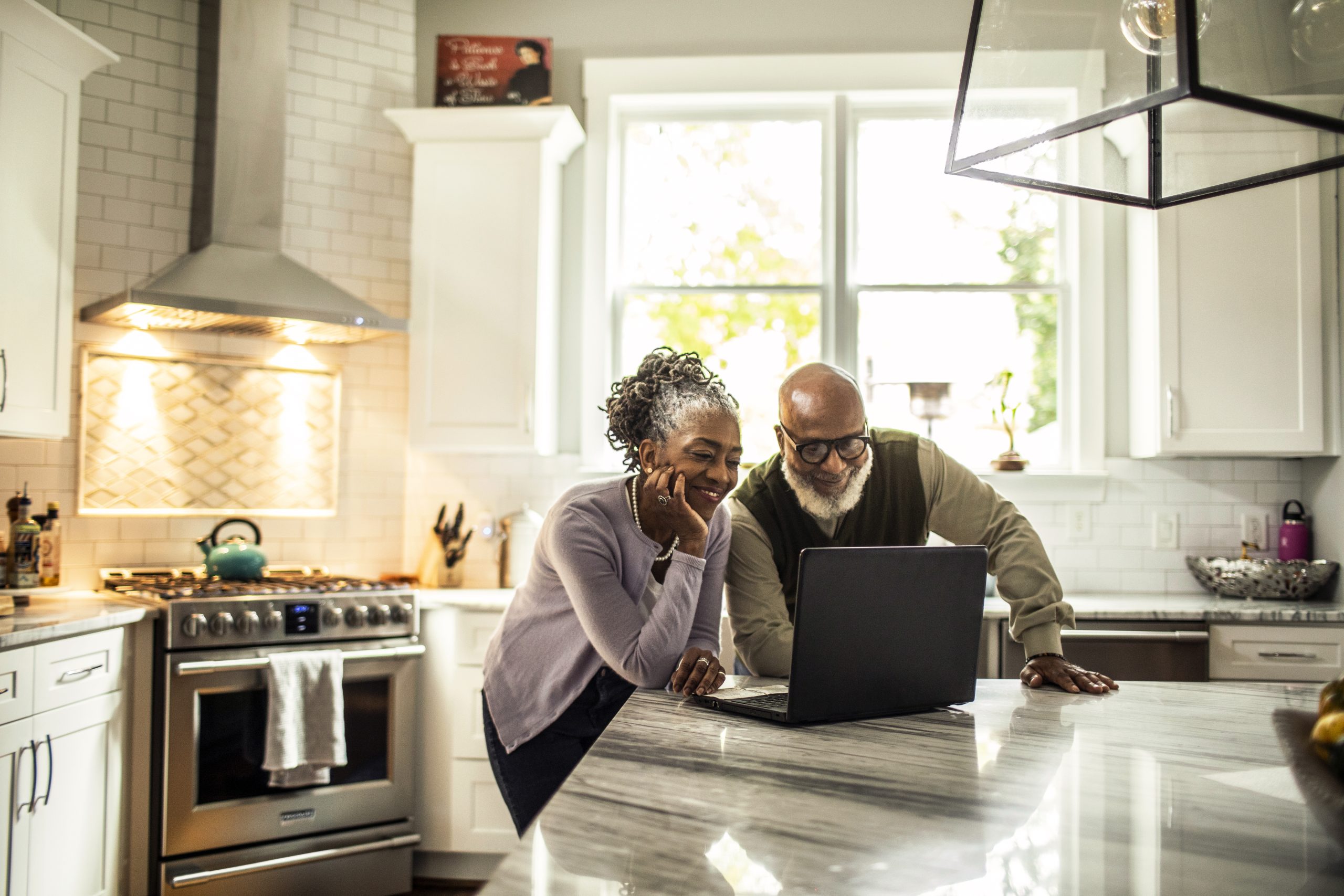 Senior couple using laptop in kitchen of suburban home