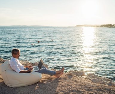 A man working on a laptop on a beach while sitting in a beanbag chair.