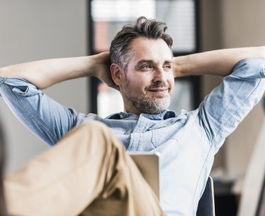 A man in business casual clothes reclines confidently with a laptop computer open on his lap.