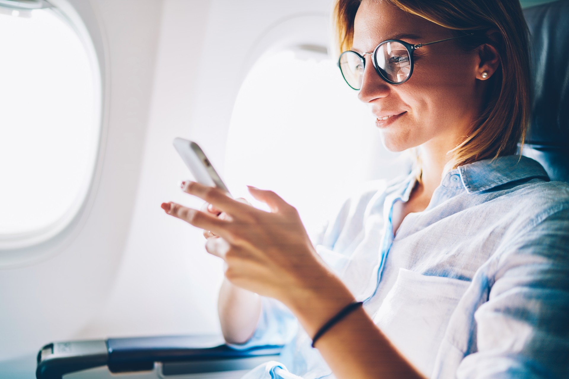 A woman looking at her phone while seated on a plane.