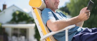 A man relaxing on a chair by a pool, looking at his phone