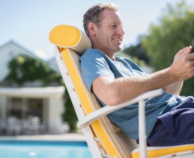 A man relaxing on a chair by a pool, looking at his phone